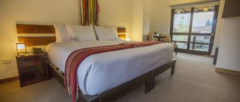 A hotel room with a large bed, a nightstand, a desk, and a window with a view.