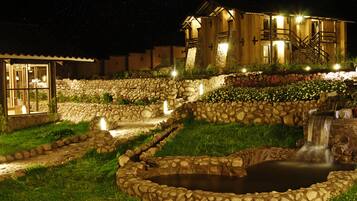 Jardín de paredes de piedra con fuente de agua y un edificio iluminado al fondo.