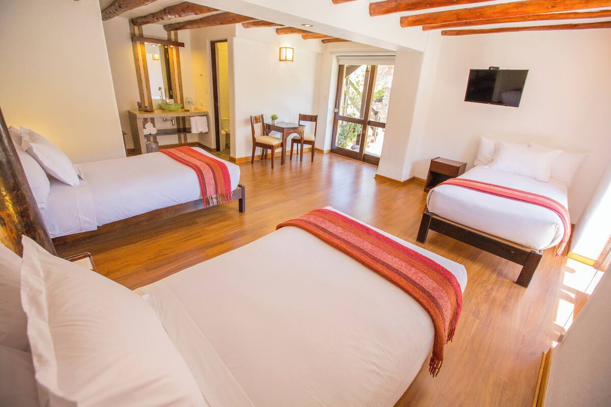 A hotel room with two beds, a bathroom, a dining area, and a TV.
