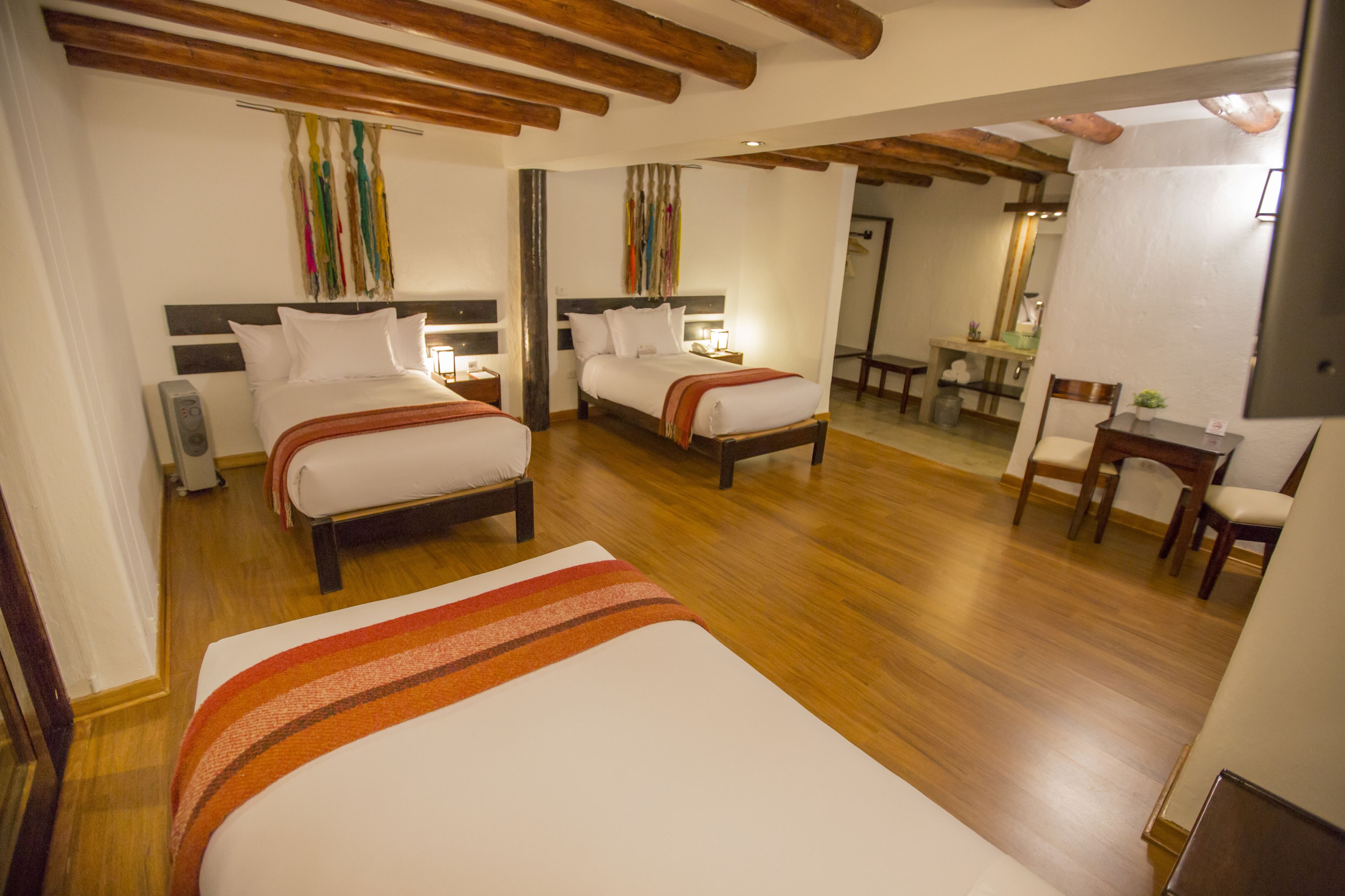 Ein Hotelzimmer mit zwei Betten, Holzboden und einem Essbereich, der durch eine offene Tür sichtbar ist.