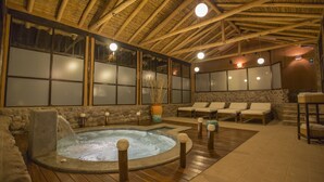 A hot tub area with wooden beams, stone walls, and lounge chairs.