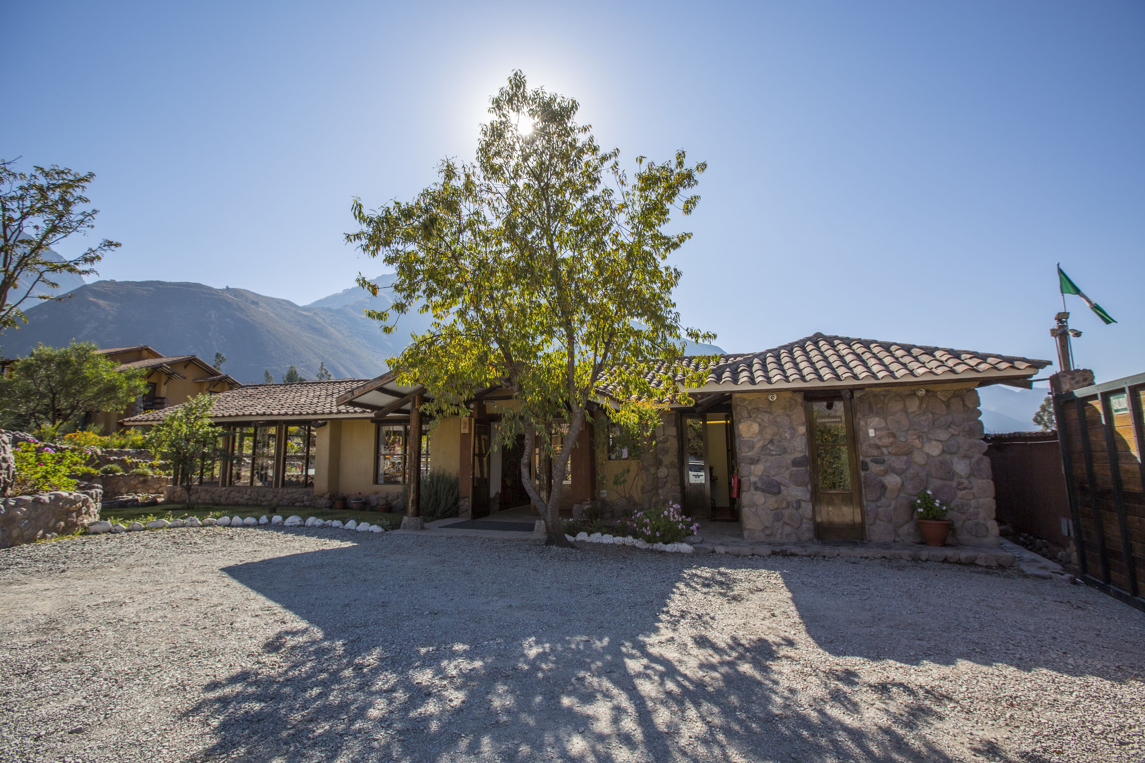 A stone building with a tiled roof, a gravel driveway, and a tree in front.