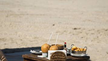 Una mesa de madera con una cesta, cocos, una bebida y aperitivos en la playa.
