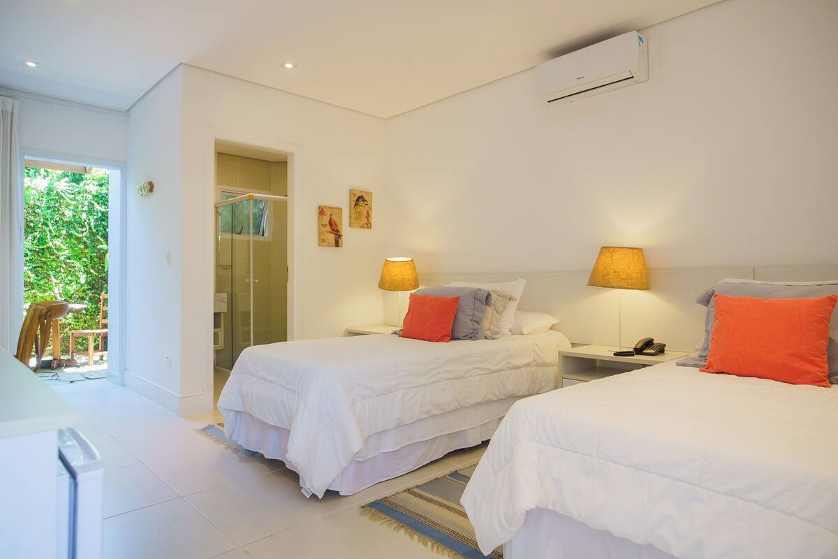 A hotel room with two beds, a sitting area, and a view of greenery outside.