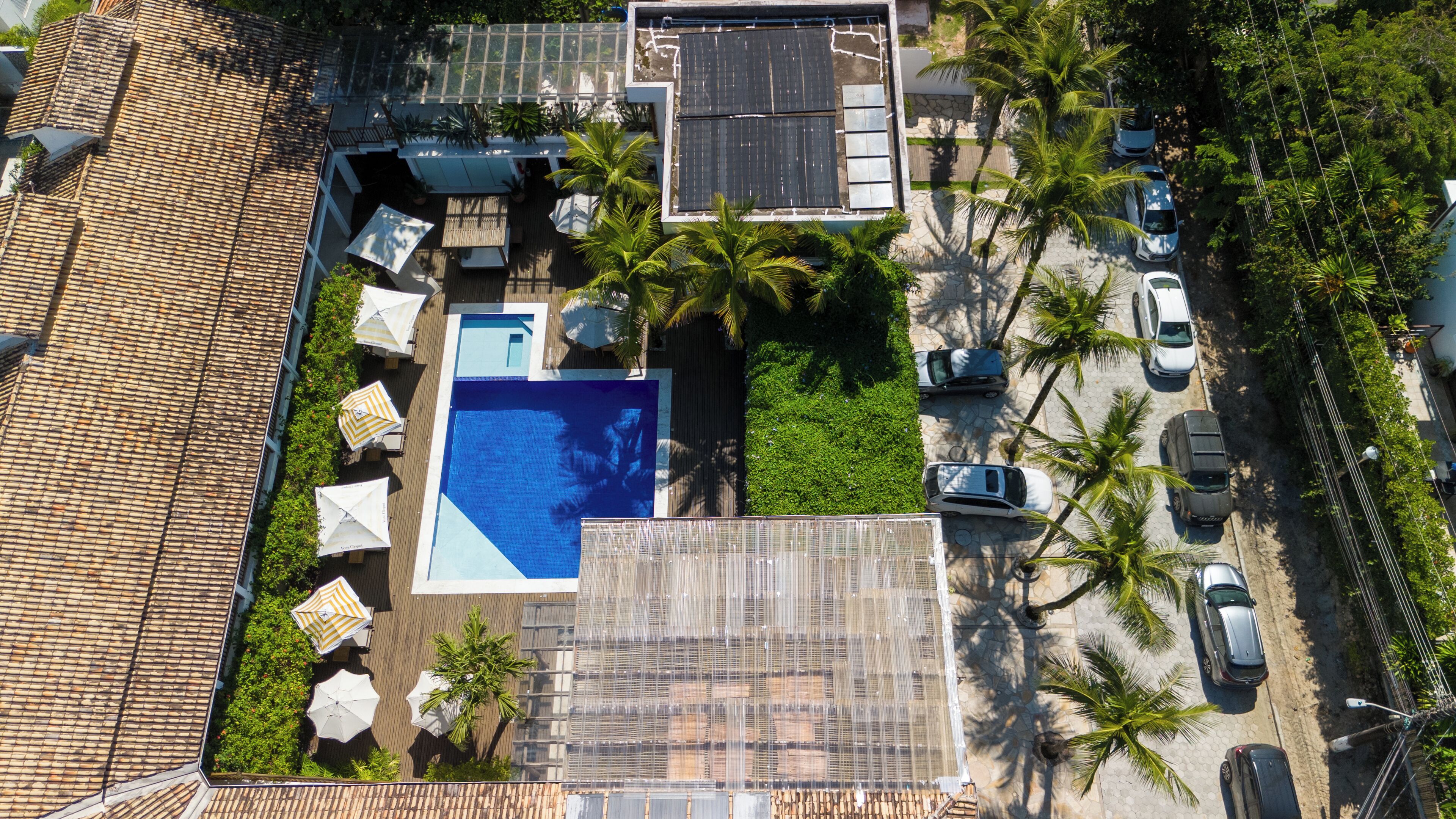 An aerial view of a residential property with a swimming pool, solar panels, and a parking area with cars.
