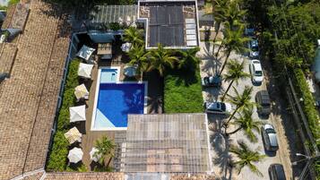 An aerial view of a residential property with a swimming pool, solar panels, and a parking area with cars.