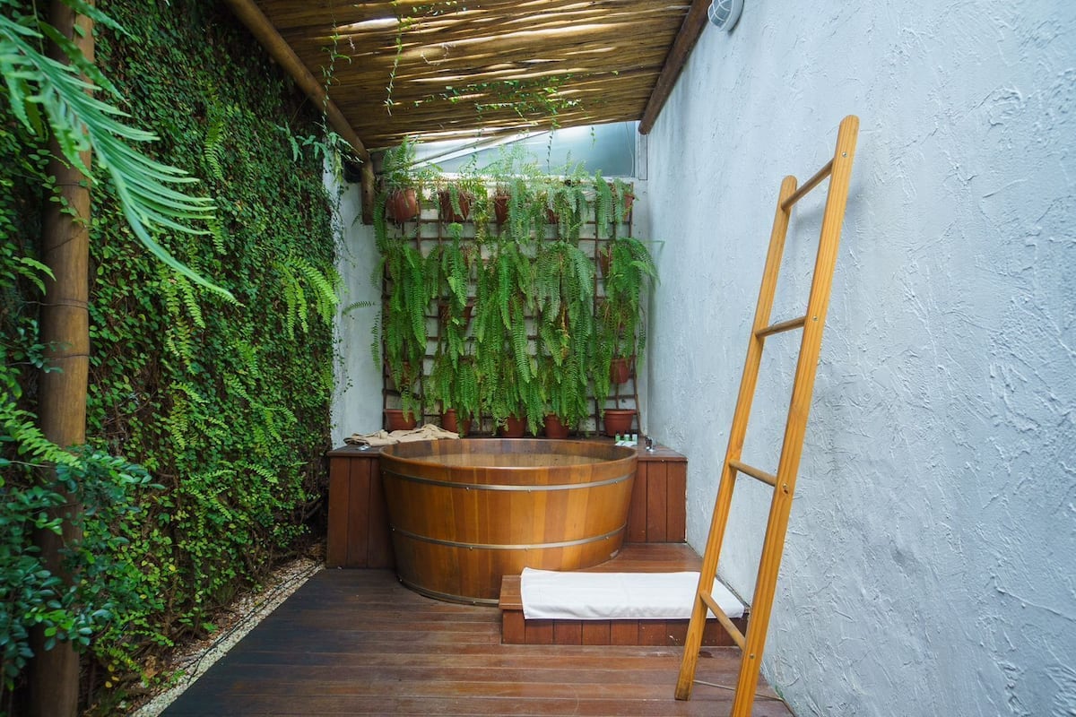 A wooden bathtub in a narrow, enclosed space with a wooden ladder and a bench.