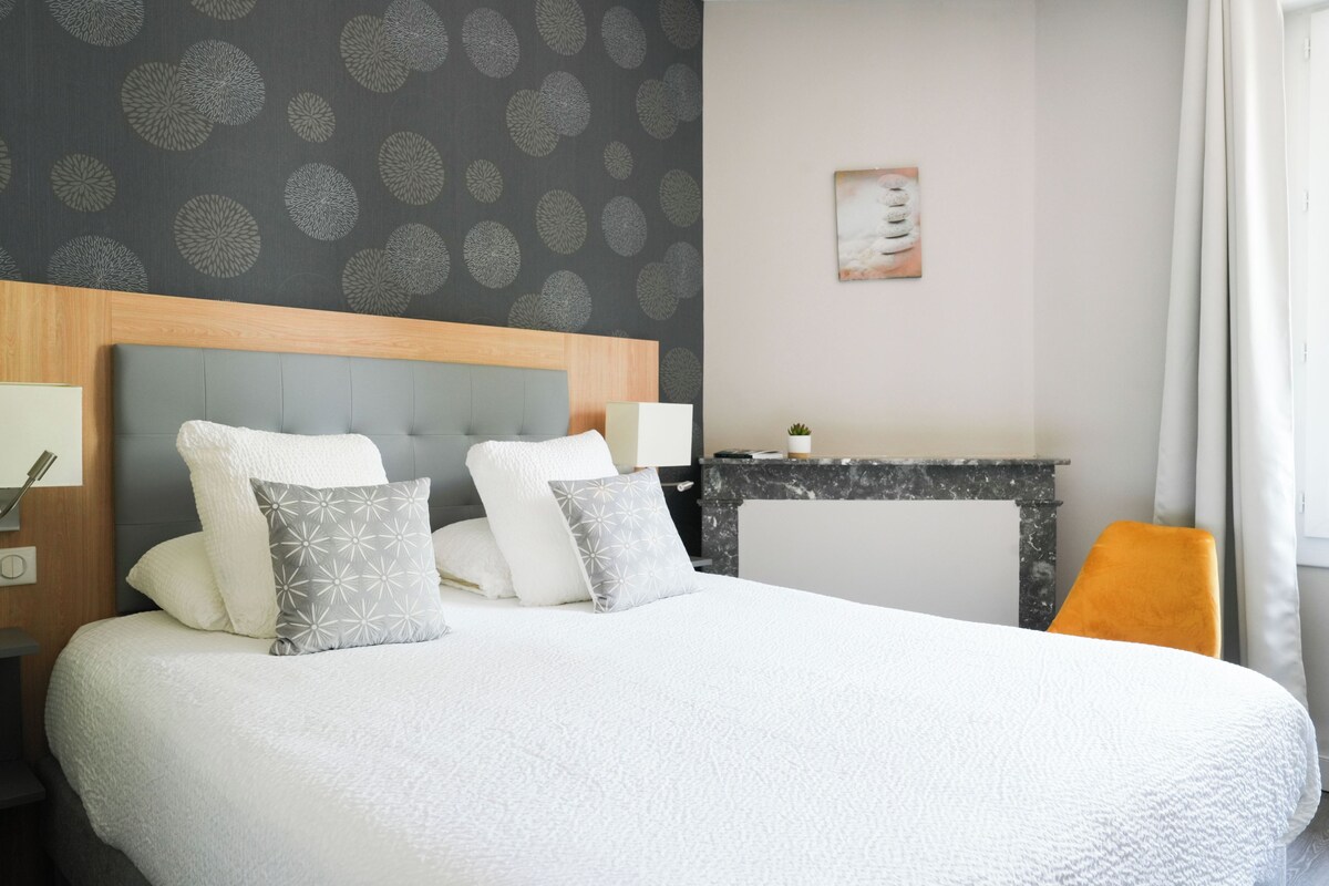 Una habitación de hotel ordenada con una cama grande, una mesita pequeña y una chimenea.