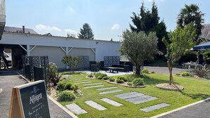 A well-maintained outdoor area with a paved patio, stone pathways, and a signboard for Affligem. - Hôtel l'Amandier (Morlaas)