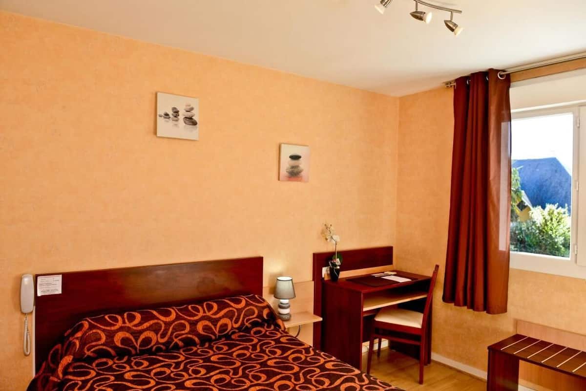 Habitación de hotel con cama, escritorio, silla y ventana con cortinas.