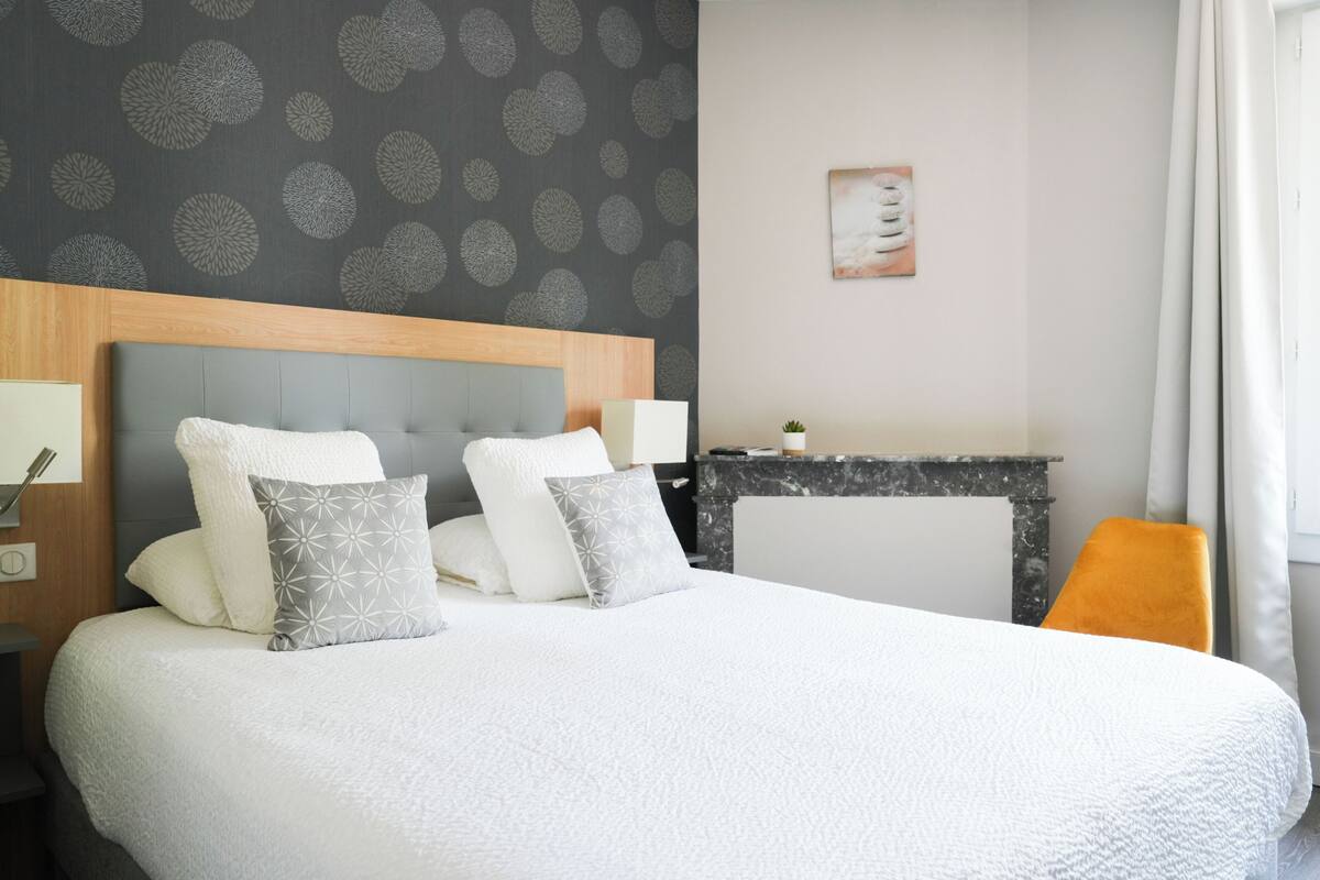 Una habitación de hotel ordenada con una cama grande, una mesita pequeña y una chimenea.