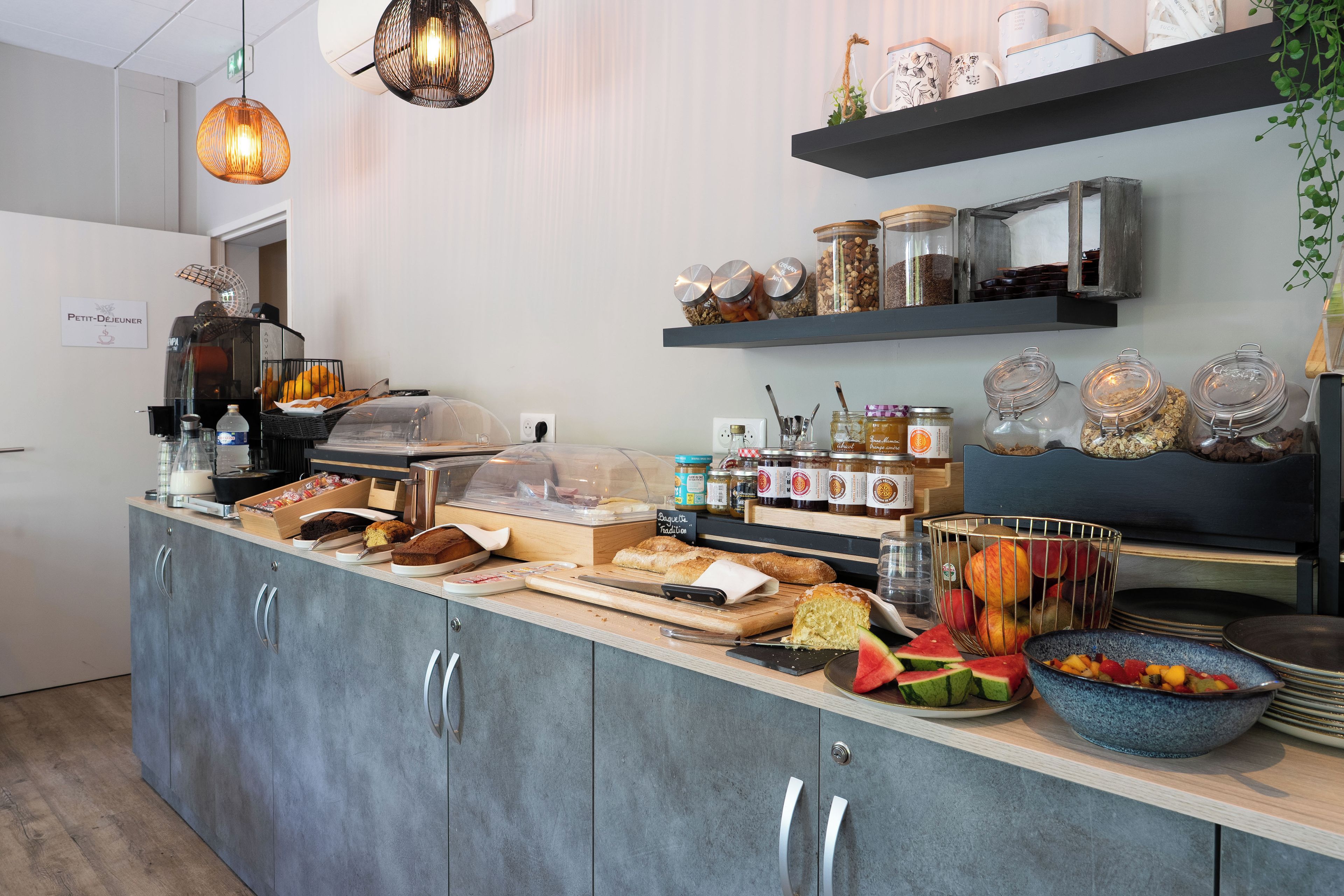 Una barra de desayuno con diversos alimentos, una máquina de café y frascos de condimentos.