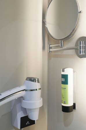 A bathroom with a toilet, a hand soap dispenser, and a mirror. - Hôtel l'Amandier (Morlaas)