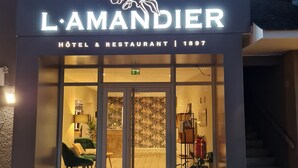The exterior of L'Amandier Hotel & Restaurant with a modern facade, large glass entrance, and a visible reception area inside. - Hôtel l'Amandier (Morlaas)