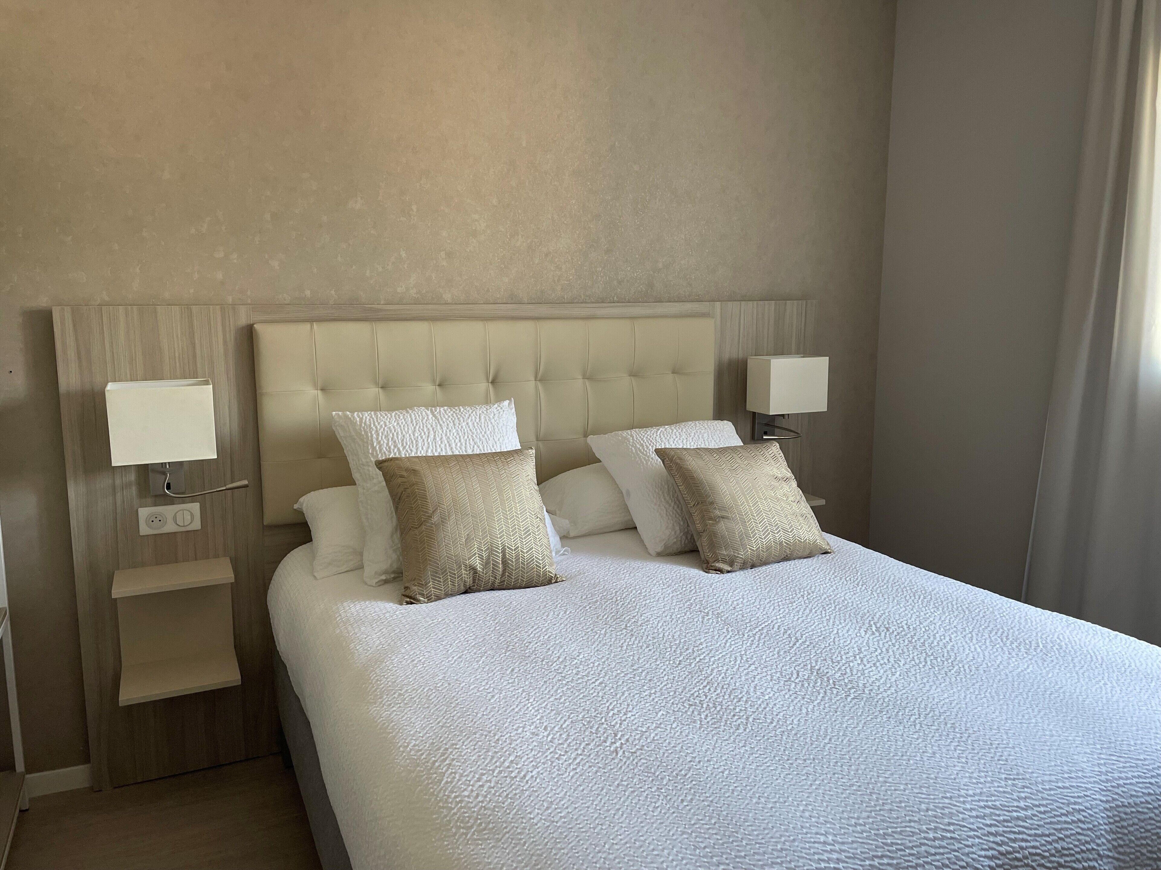 A hotel room with a large bed, two bedside lamps, and a nightstand with a lamp.