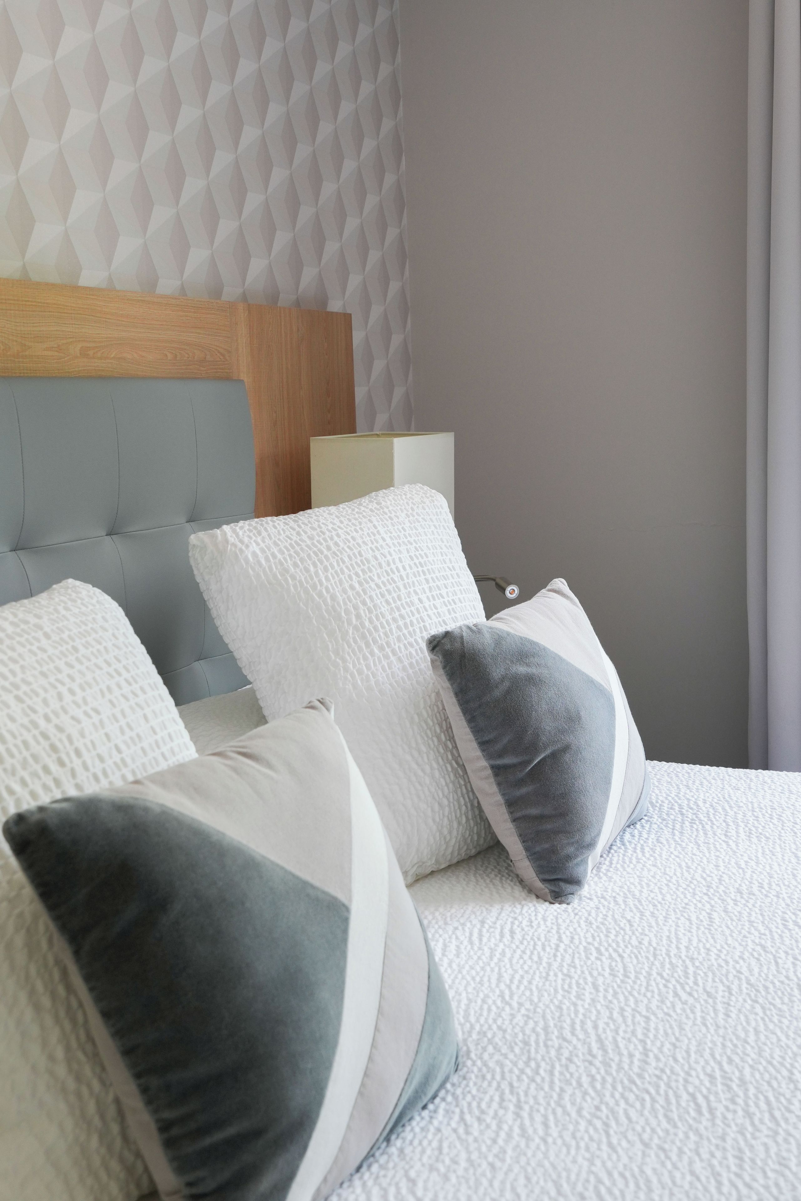 A neatly made bed with a headboard, multiple pillows, and a bedside table with a lamp.