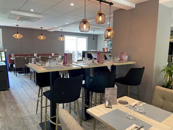 A restaurant with multiple tables, black chairs, and hanging pendant lights.