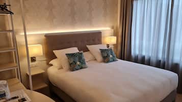 Een net opgemaakt bed met witte lakens, twee decoratieve kussens, een nachtkastje met een lamp en een bijtafeltje met een lamp.