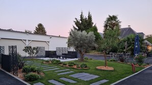A well-maintained garden with a paved pathway, seating area, and a variety of trees and shrubs. - Hôtel l'Amandier (Morlaas)