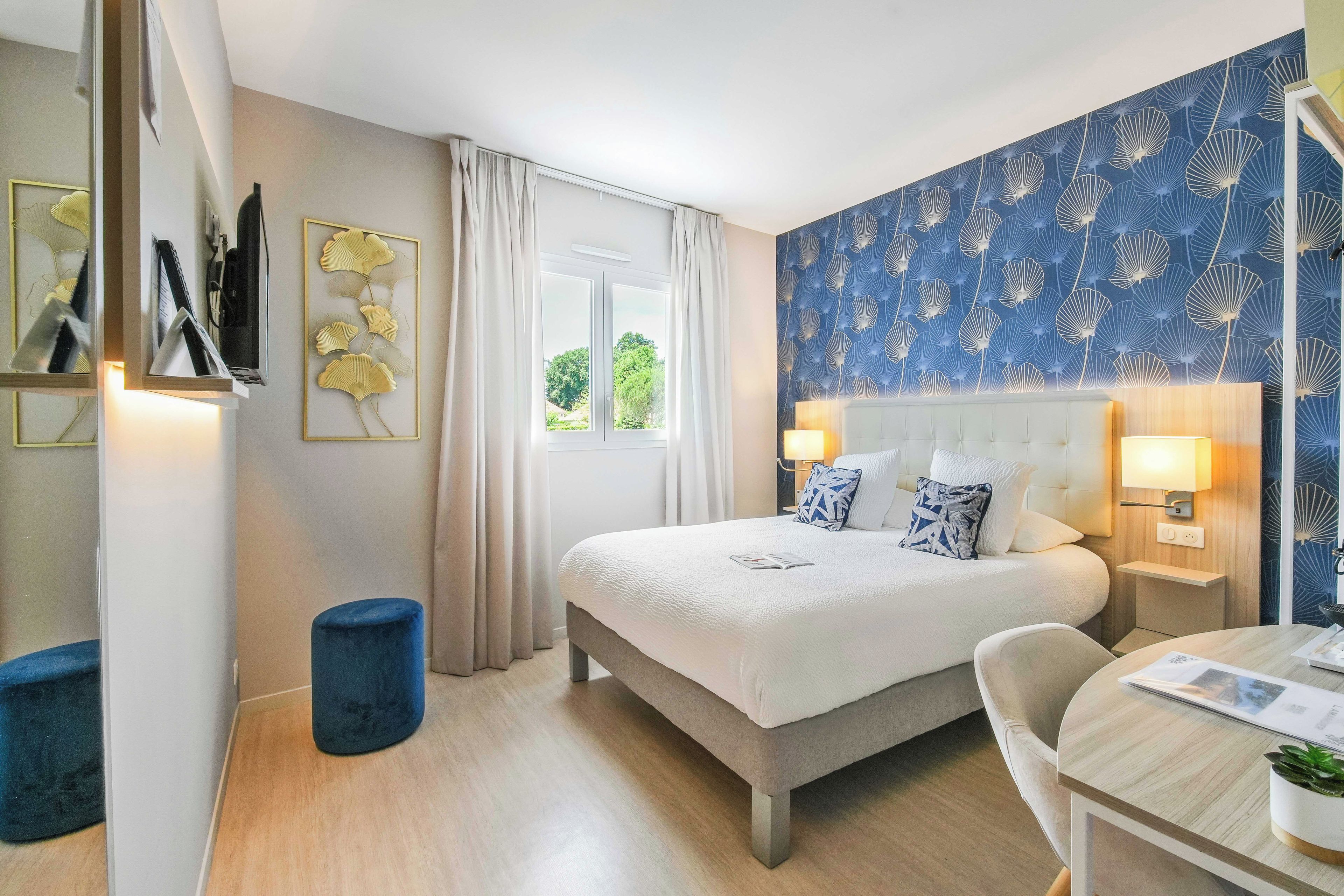 Une chambre d’hôtel avec un lit, des tables de chevet, une chaise, une petite table et une fenêtre avec des rideaux.
