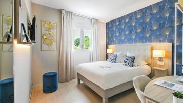 Une chambre d’hôtel avec un lit, des tables de chevet, une chaise, une petite table et une fenêtre avec des rideaux.