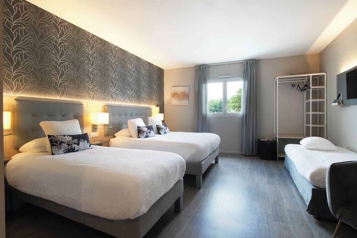 Habitación de hotel con dos camas, un armario, un espejo y una ventana con cortinas.