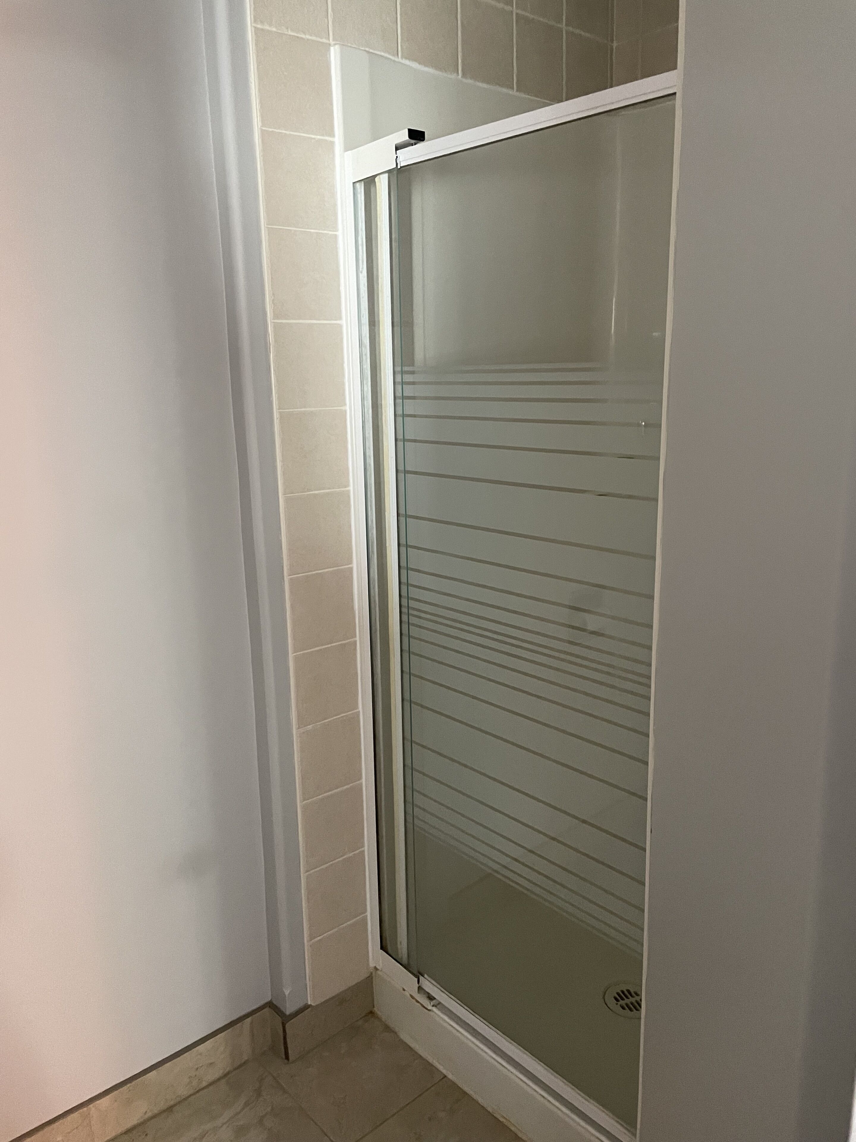 Esquina de un cuarto con una puerta de ducha de vidrio y pared de azulejos blancos.
