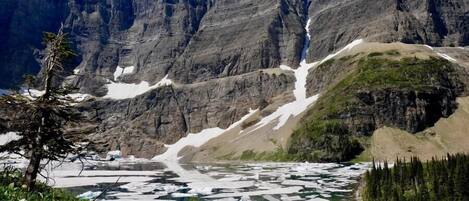 A mountainous landscape with a river flowing through a valley, surrounded by rocky cliffs and sparse vegetation.