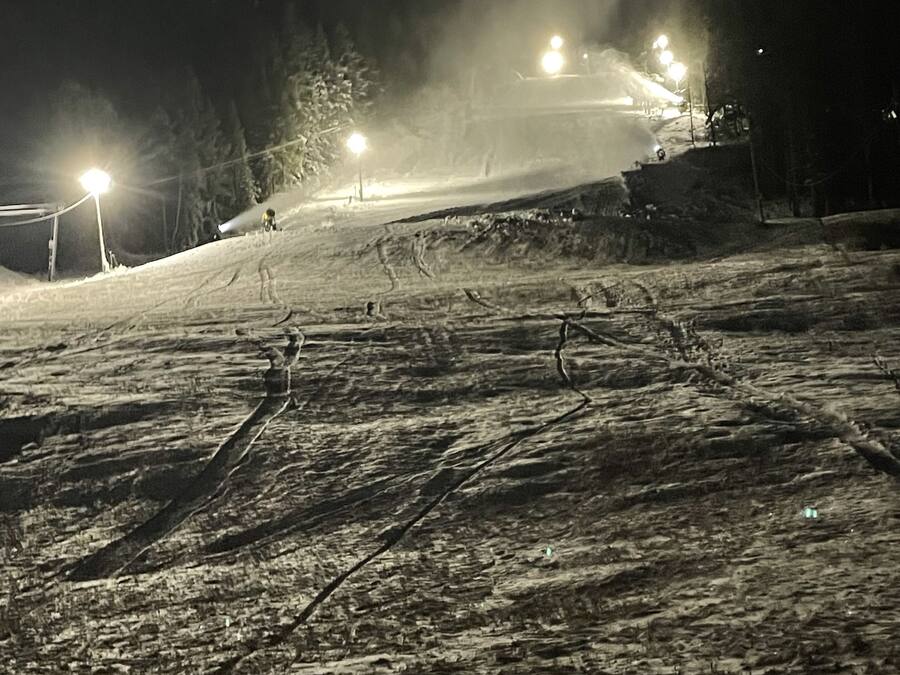A snow-covered slope with ski tracks and artificial lighting.