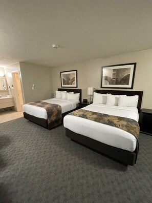 A hotel room with two beds, a bathroom, and two framed pictures on the wall. - BCMInns Coleman (Coleman)