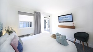 Habitación de hotel con una cama grande, un televisor montado en la pared, un pequeño espacio de descanso y vistas al exterior a través de una puerta corrediza.