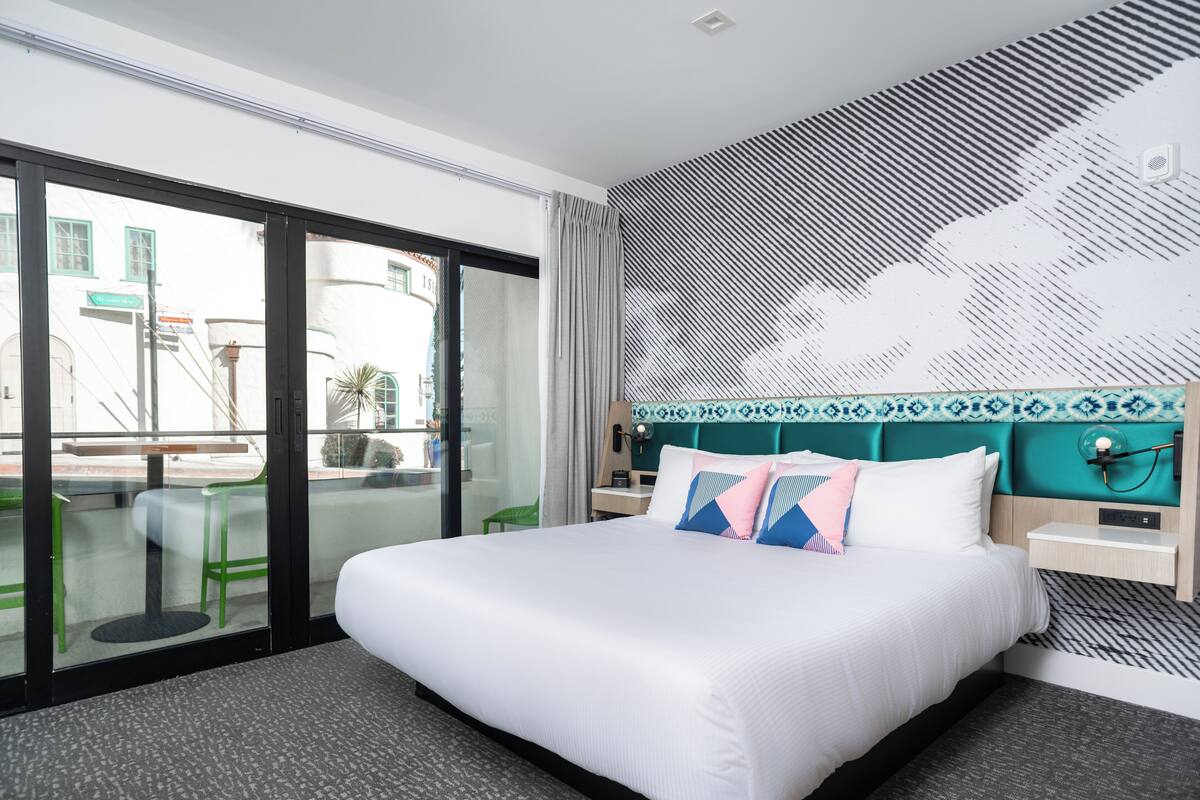 A modern hotel room with a large bed, a view through a glass door, and a patterned wall.
