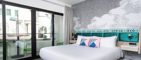 A modern hotel room with a large bed, a view through a glass door, and a patterned wall.