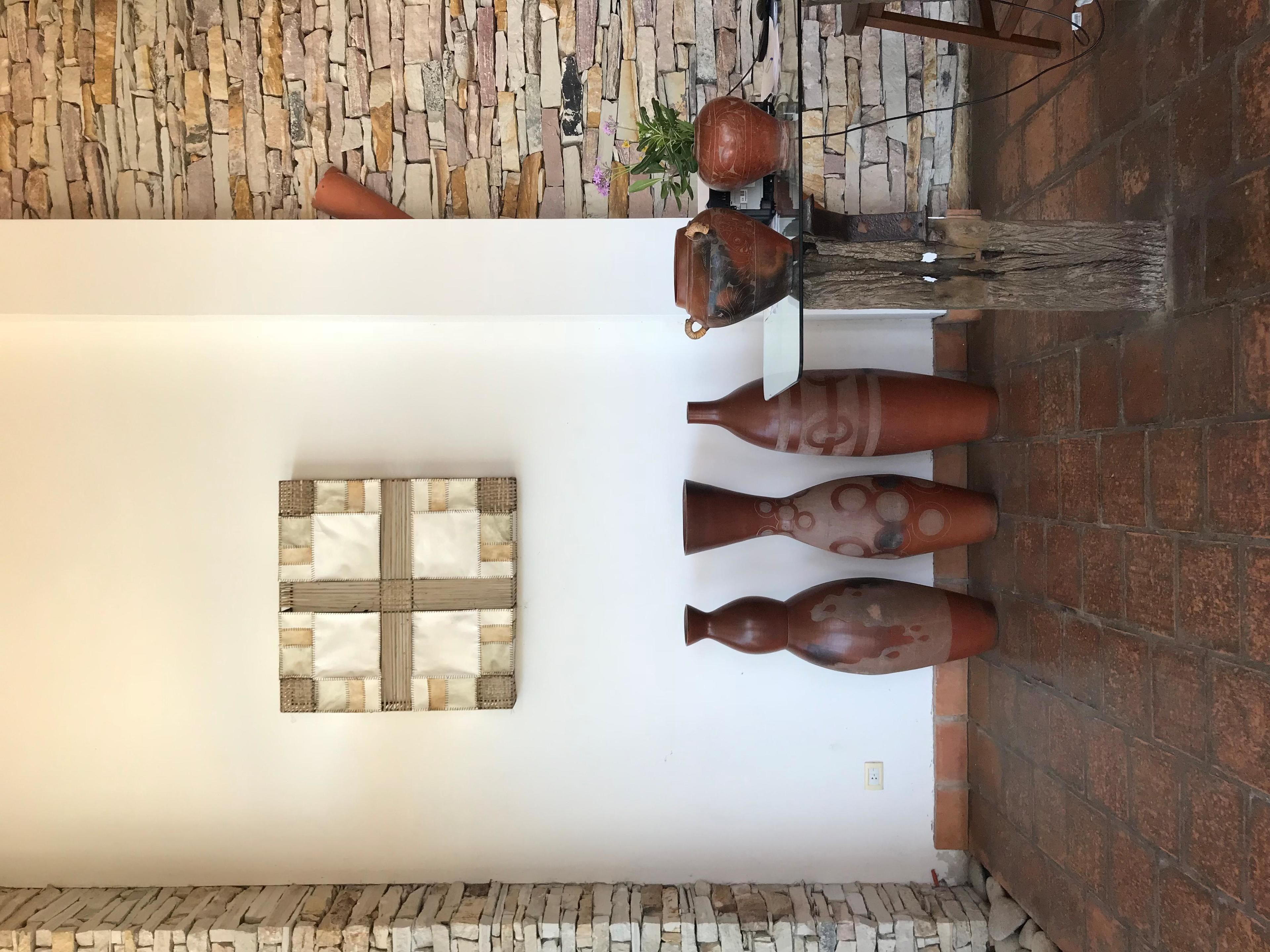 Ein Zimmer mit weißer Wand, Steinwand und Fliesenboden. Auf einem Tisch stehen drei große Vasen und an der Wand ein Blumentopf.