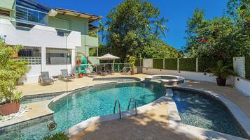 A swimming pool with a sun deck, lounge chairs, and a covered seating area.