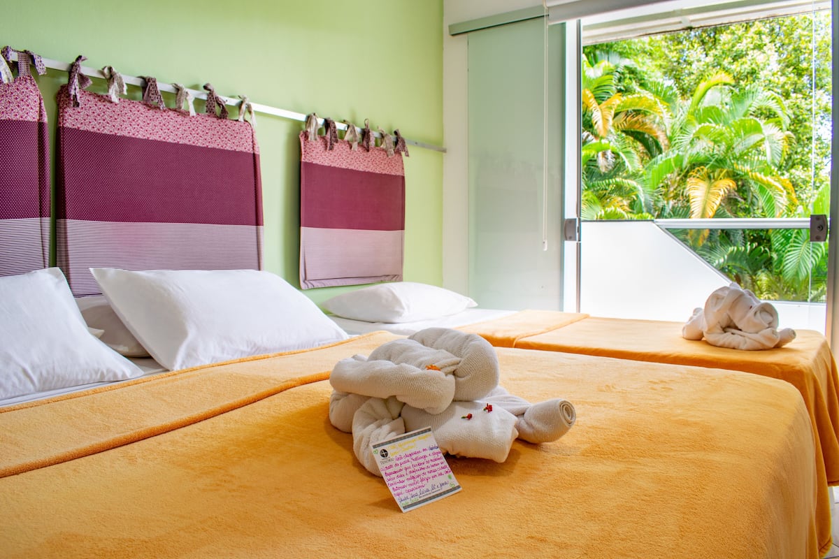 Habitación de hotel con dos camas, cada una con una toalla enrollada y una almohada. Hay un cartel sobre la cama.