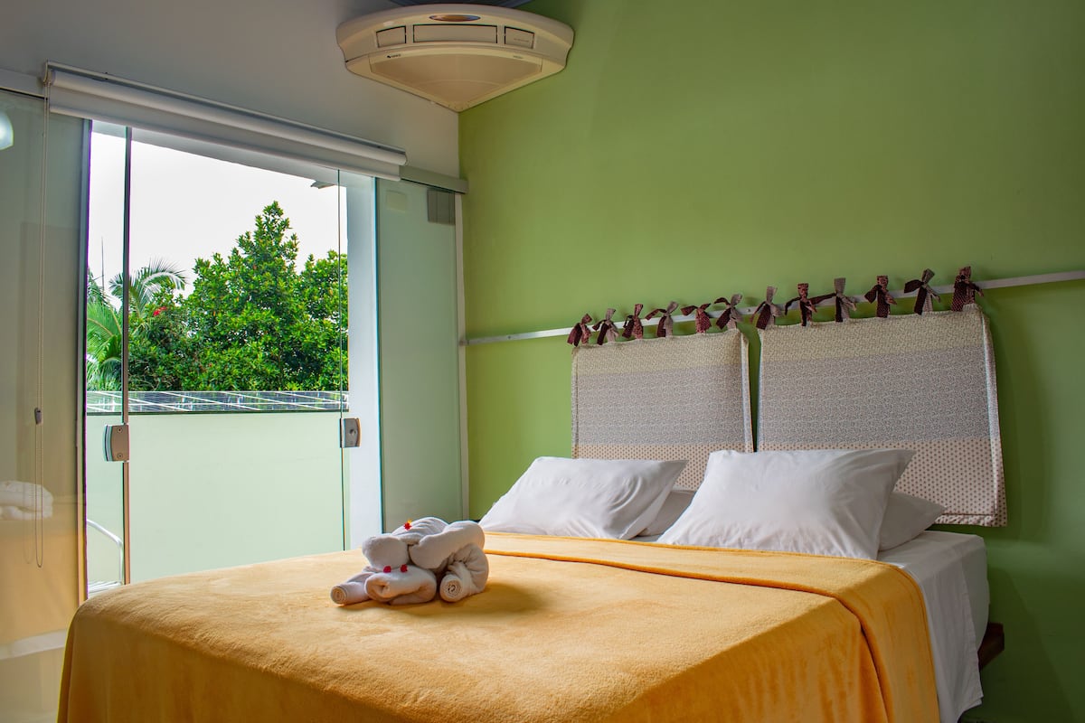 Una habitación de hotel con cama, ventana que da a zonas verdes y una lámpara en el techo.