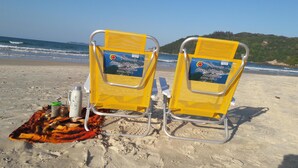 Dos sillas de playa amarillas con una toalla y un termo sobre la arena.