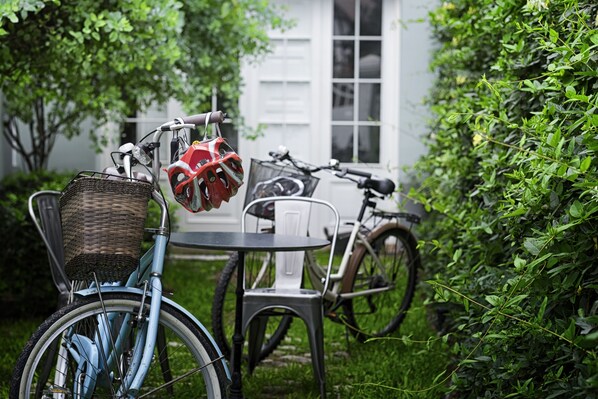 A bicycle with a basket and helmet, a table, and chairs in a garden area with a white building in the background.