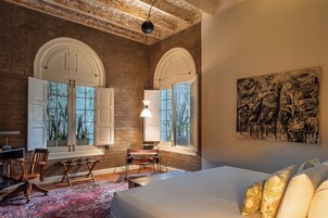 Ein Schlafzimmer mit einem großen Bett, zwei Fenstern mit weißen Fensterläden, einem Schreibtisch mit Stuhl und einem Bild an der Wand.