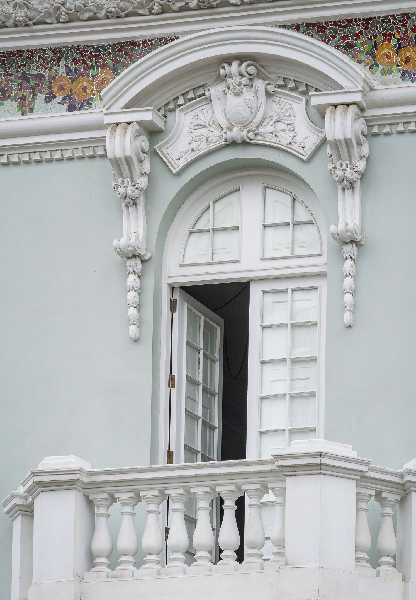 A building with a white arched window, ornate white balustrade, and a decorative ceiling with floral mosaic.