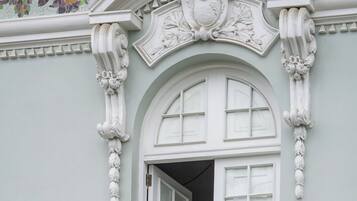 A building with a white arched window, ornate white balustrade, and a decorative ceiling with floral mosaic.