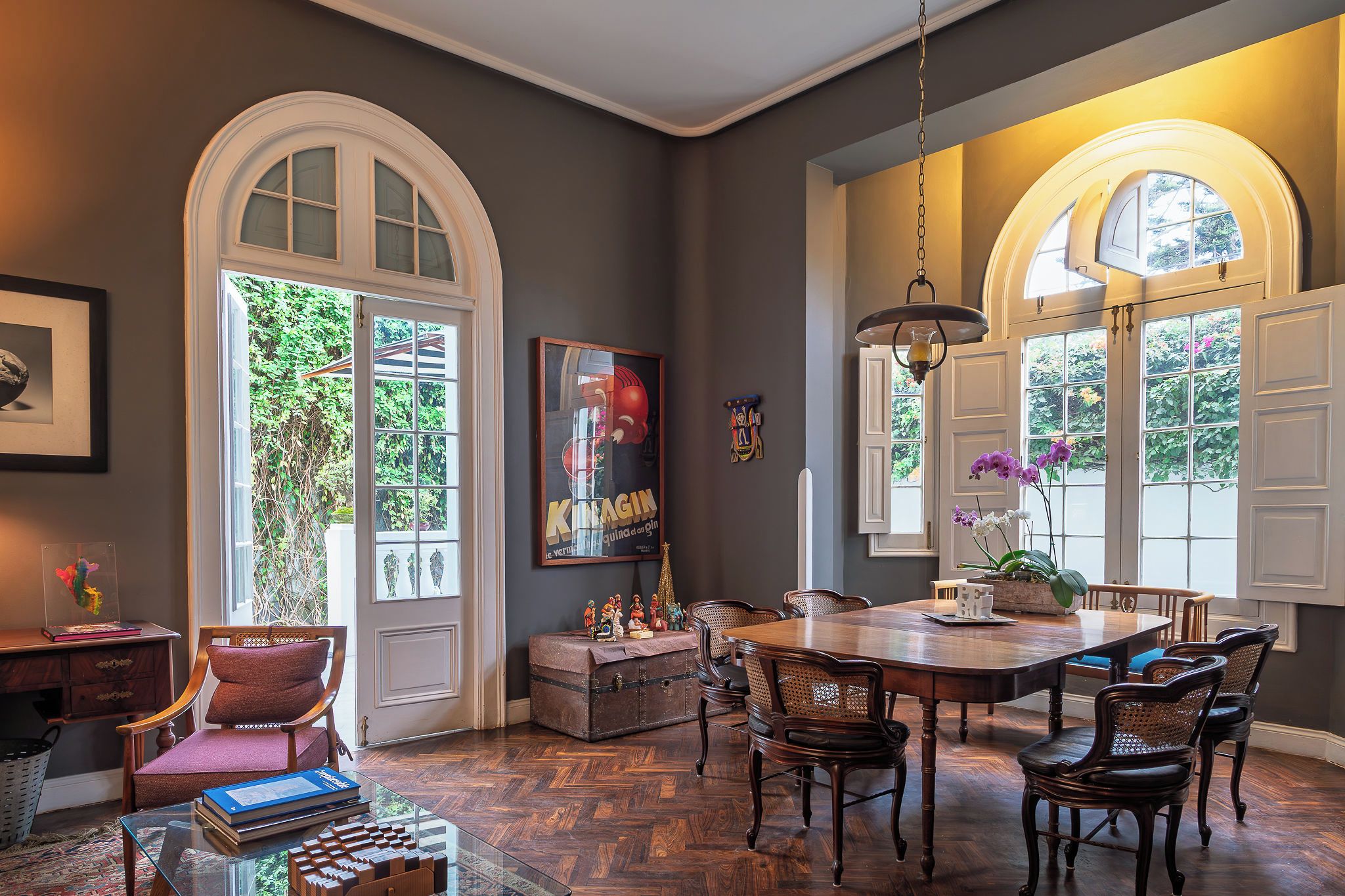 Un comedor con mesa y sillas de madera, una araña y vistas al exterior con vegetación.