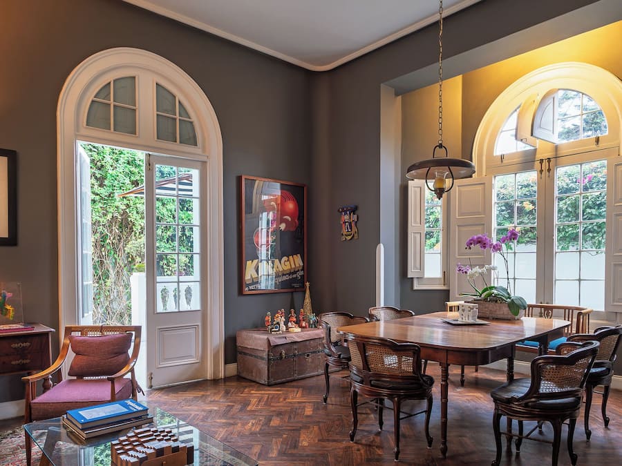Un comedor con mesa y sillas de madera, una araña y vistas al exterior con vegetación.