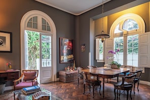 A dining area with a wooden table and chairs, a chandelier, and a view of greenery outside. - Villa Barranco by Ananay Hotels (Lima)