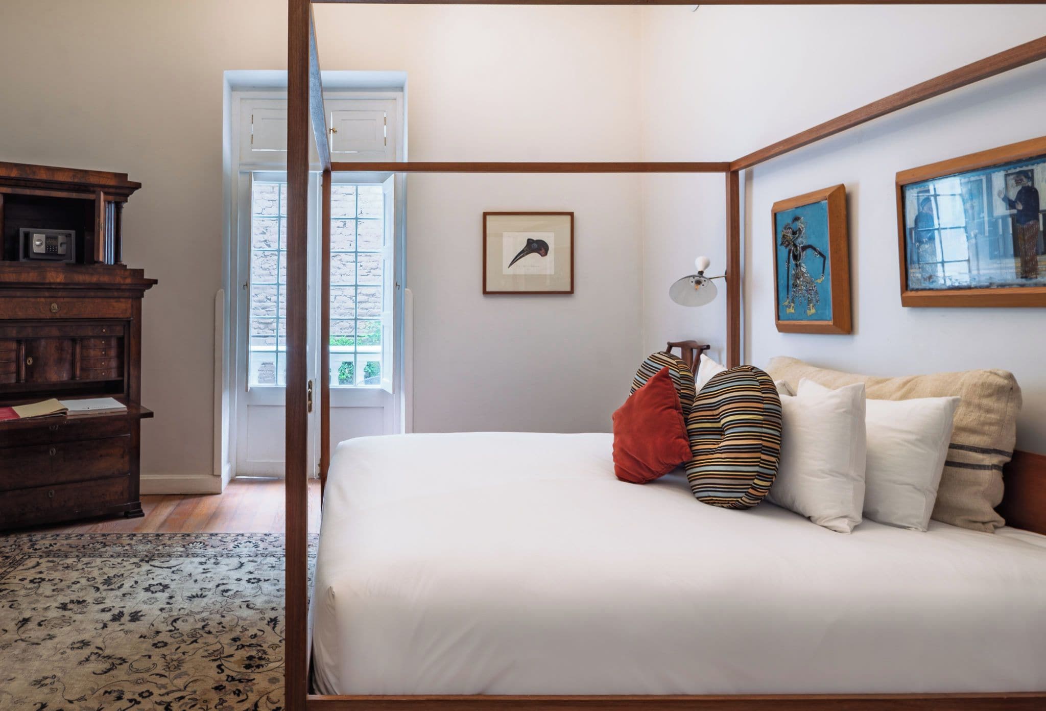 Un dormitorio con cama con dosel, cómoda de madera, un cuadro enmarcado en la pared y ventana con vistas al exterior.
