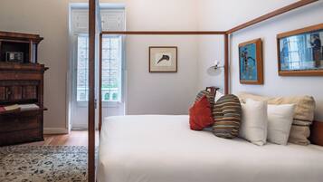 Un dormitorio con cama con dosel, cómoda de madera, un cuadro enmarcado en la pared y ventana con vistas al exterior.
