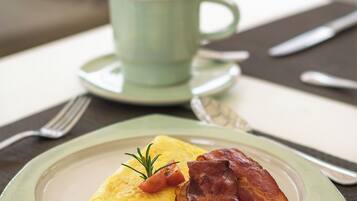 Un plato con tortilla, tocino y una ramita de romero, acompañado por una taza de café sobre una mesa.