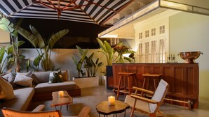Un rincón acogedor con un sofá, sillones, una mesita con una vela, y una zona de bar con taburetes y un cuenco de cobre.