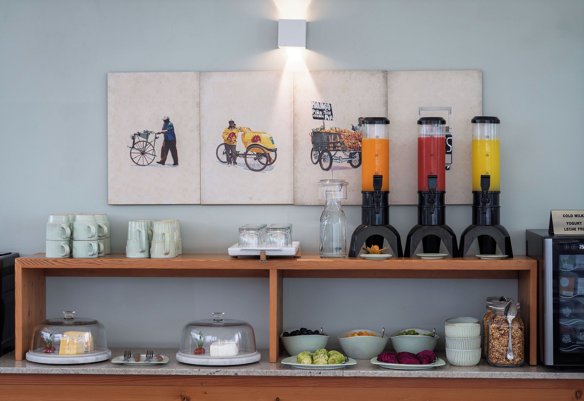 Een ontbijtbalk met een wandlamp, een assortiment mokken, glazen en een koelkast met koude melk en yoghurt.